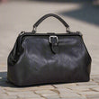 Load image into Gallery viewer, Black leather handbag on a light wooden surface