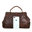 Load image into Gallery viewer, Brown leather handbag with a white phone inside on a wooden surface