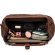 Load image into Gallery viewer, Open brown leather duffel bag with travel items on a beige background