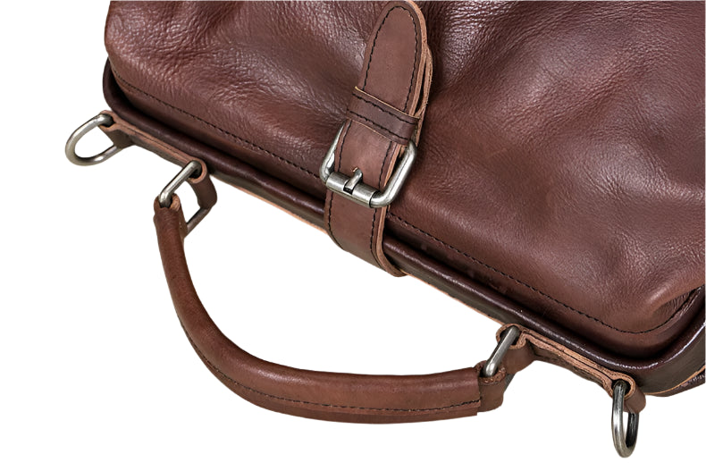 Brown leather bag with metal hardware on a light wooden surface