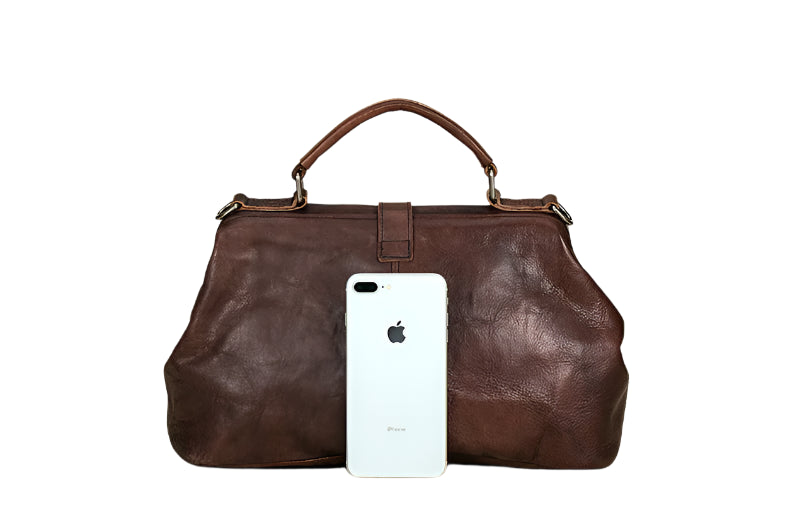 Brown leather handbag with a white phone inside on a wooden surface