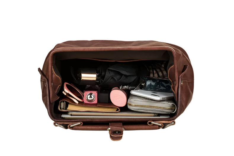 Open brown leather duffel bag with travel items on a beige background